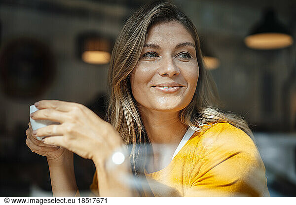 Smiling woman with coffee cup in cafe seen through glass
