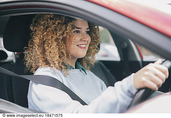 Smiling woman with curly hair driving car