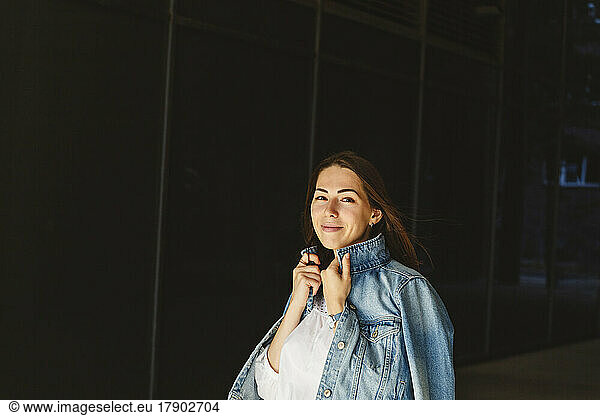 Smiling woman with denim jacket in front of black wall