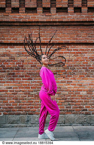 Smiling woman with dreadlocks standing in front of brick wall