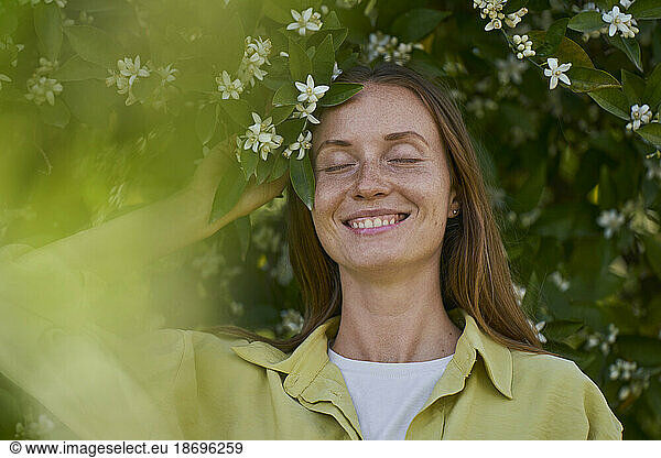Smiling woman with eyes closed by orange blossom flower in garden