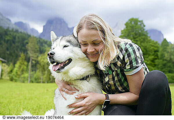 Smiling woman with eyes closed embracing Husky dog
