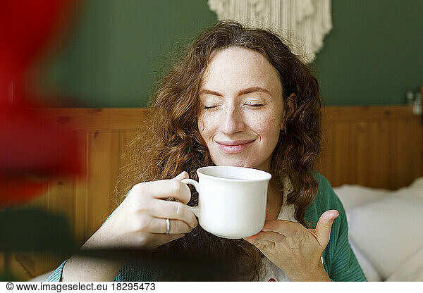 Smiling woman with eyes closed having tea at home