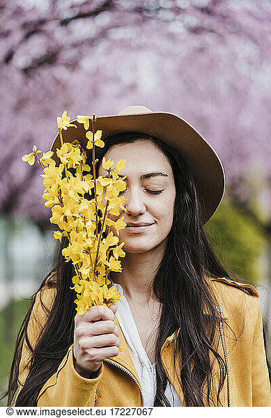 Smiling woman with eyes closed holding yellow flowers during springtime