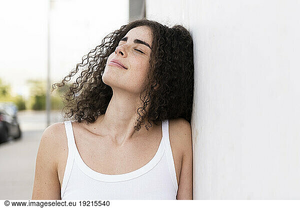 Smiling woman with eyes closed leaning on wall