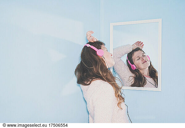 Smiling woman with eyes closed listening music through headphones in front of mirror at home