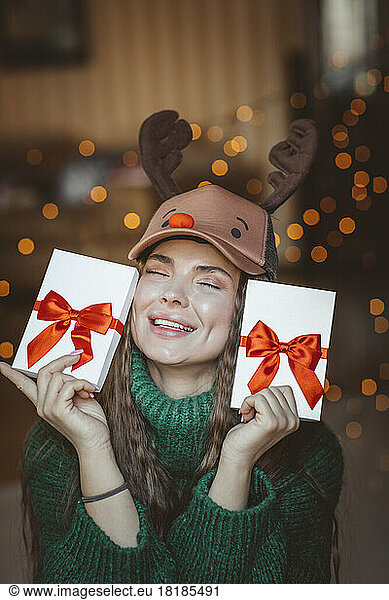 Smiling woman with eyes closed showing Christmas presents at home