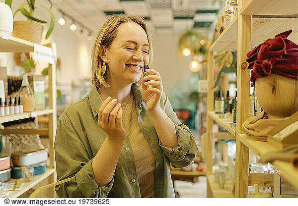 Smiling woman with eyes closed smelling face oil in zero waste store