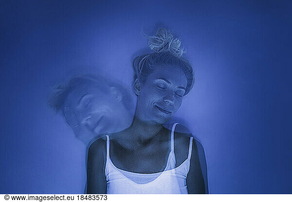 Smiling woman with eyes closed under UV light against blue background