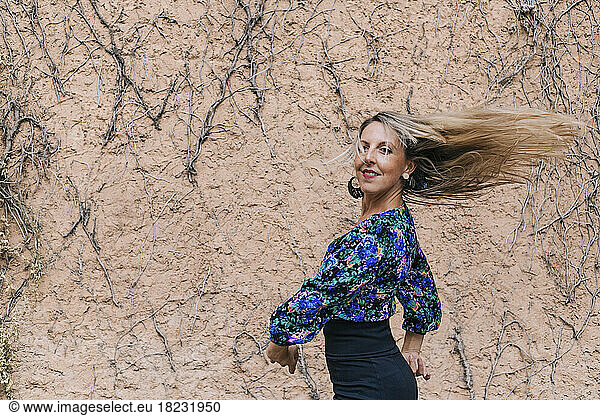 Smiling woman with hair tossed dancing in front of wall