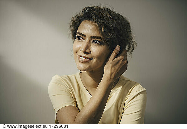 Smiling woman with hand in hair against beige wall