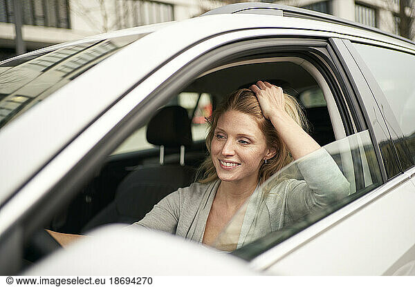 Smiling woman with hand in hair driving car