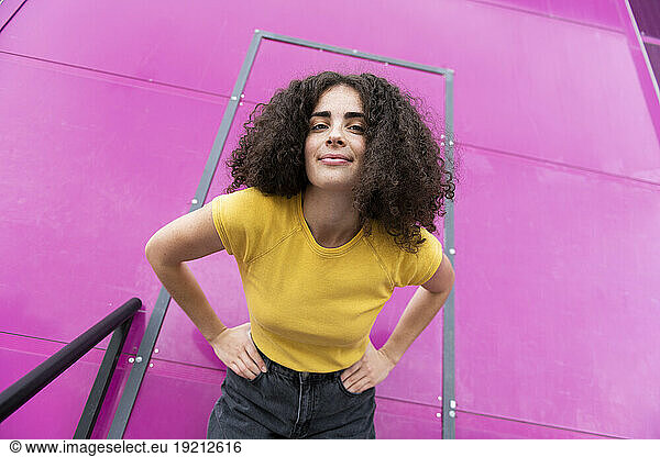 Smiling woman with hands on hip standing in front of pink door