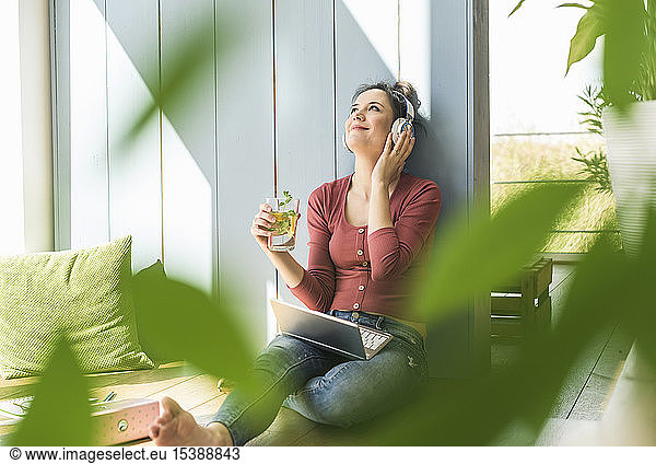 Smiling woman with headphones and laptop sitting at the window at home