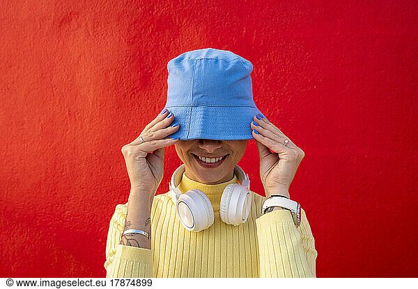 Smiling woman with headphones covering face with blue bucket hat