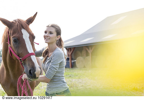 Smiling woman with horse outside rural barn