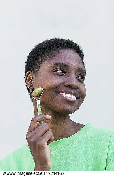 Smiling woman with jade roller against white background