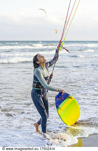 Smiling woman with kiteboard looking up at kite parachute