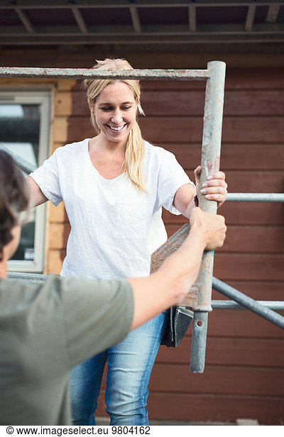 Smiling woman with man working on scaffolding outside house being renovated
