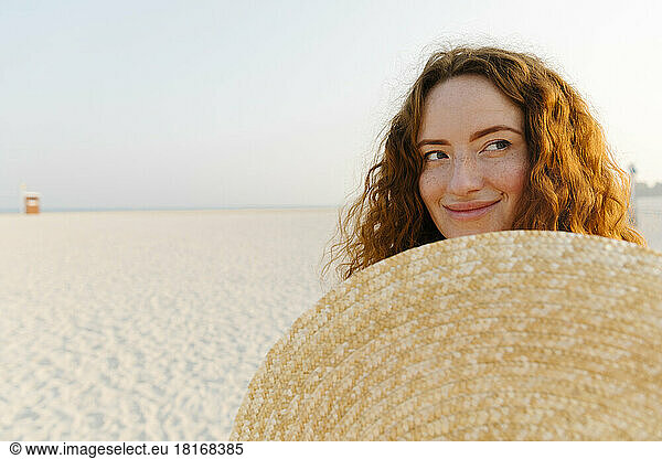 Smiling woman with oversized straw hat at beach