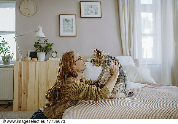 Smiling woman with pet dog leaning on bed at home