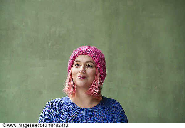 Smiling woman with pink dyed hair in front of green wall