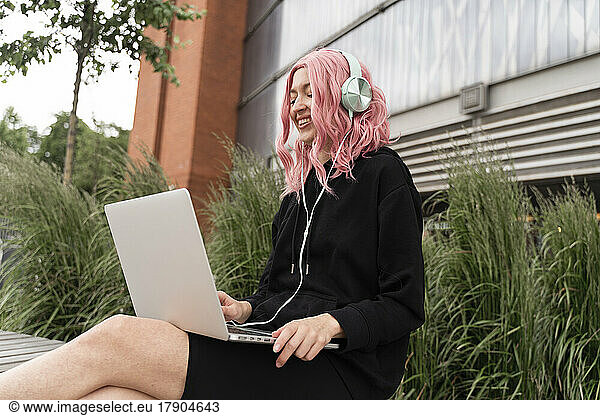 Smiling woman with pink hair listening music through headphones