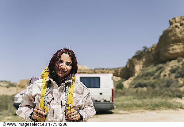 Smiling woman with red hair wearing backpack on sunny day