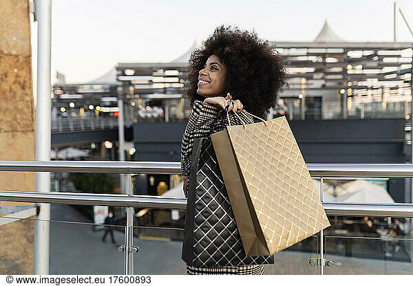 Smiling woman with shopping bags walking by railing