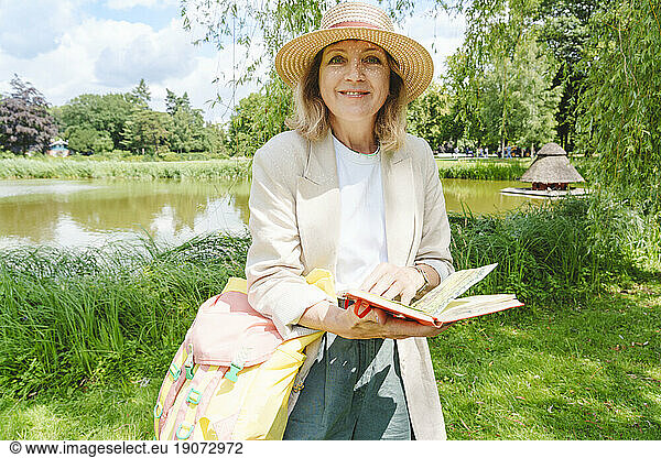 Smiling woman with sketch pad standing in park on sunny day