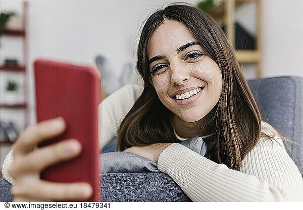 Smiling woman with smart phone lying on sofa at home