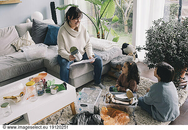 Smiling woman with son and daughter separating waste while sitting in living room