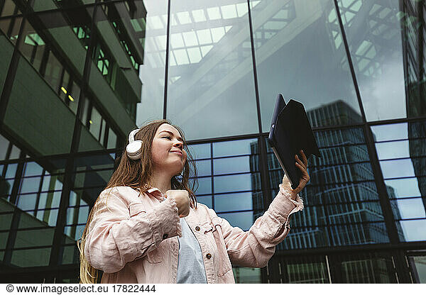 Smiling woman with tablet PC in front of glass building