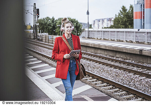 Smiling woman with tablet PC walking on railroad station platform
