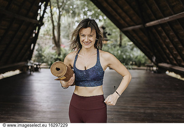 Smiling woman with yoga mat at hut