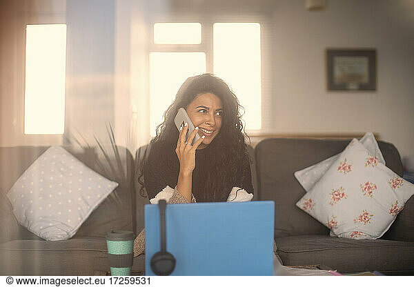 Smiling woman working from home talking on smart phone at laptop