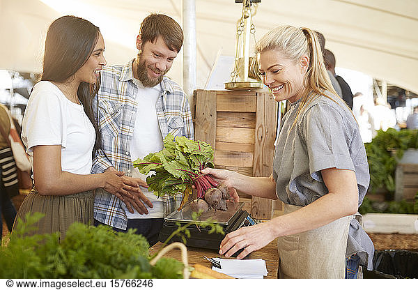 Smiling woman working  helping couple at farmerâ€™s market