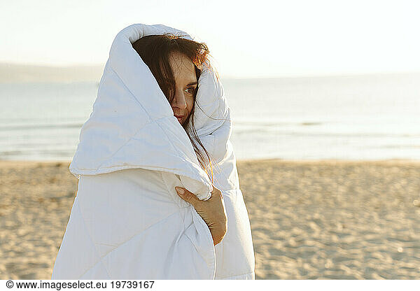 Smiling woman wrapped in blanket standing at beach