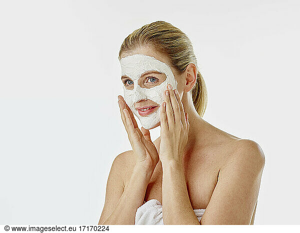 Smiling woman wrapped in towel applying face mask