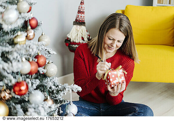 Smiling woman writing with pen on Christmas present at home