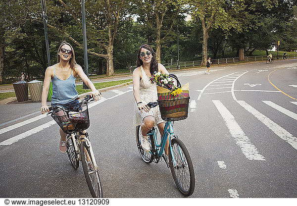 Smiling women cycling on city street against trees