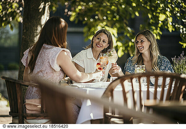 Smiling women enjoying drinks sitting at dining table in restaurant