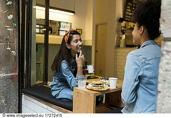 Smiling women talking while sitting by window at cafe
