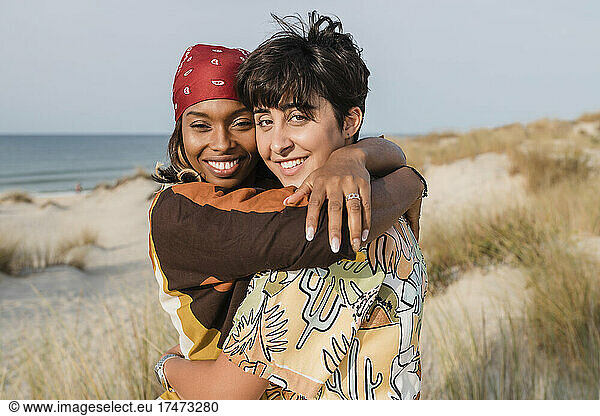 Smiling women with bandana embracing lesbian friend at beach