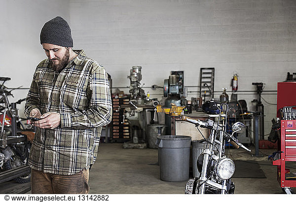 Smiling worker using phone while standing at auto repair shop