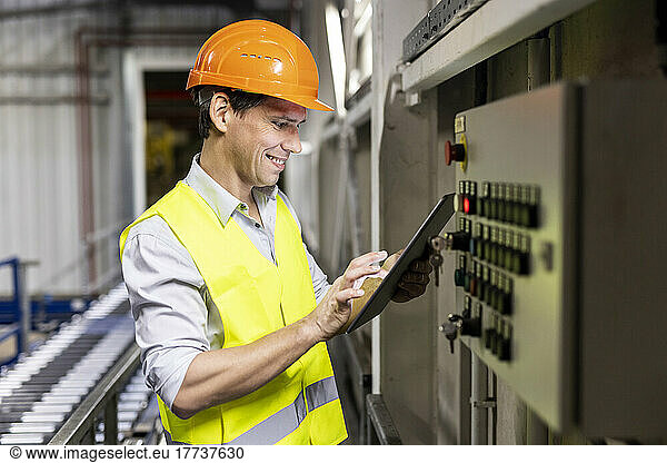 Smiling worker using tablet PC by control panel in warehouse