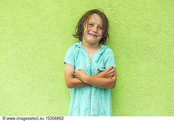 Smiling 5 year old boy posing in front of green wall