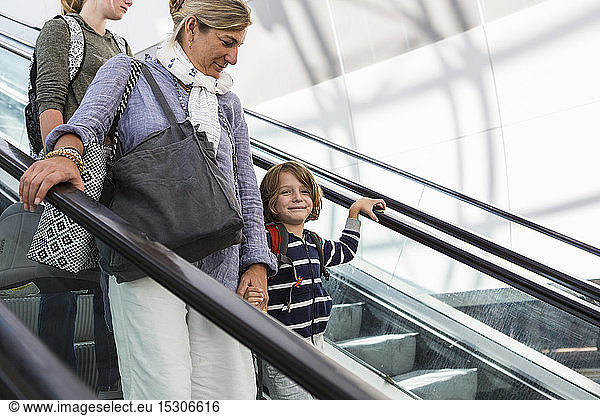 Smiling 5 year old boy traveling on airport escalator with his mother and older sister