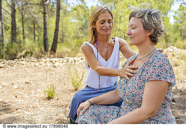 Smiling yoga instructor teaching meditation to friend on sunny day