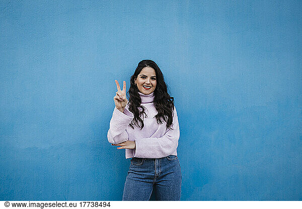 Smiling young beautiful woman showing number 2 in front of blue wall